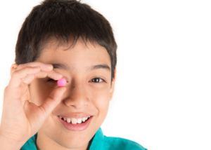 child's face holding small pill by his eye